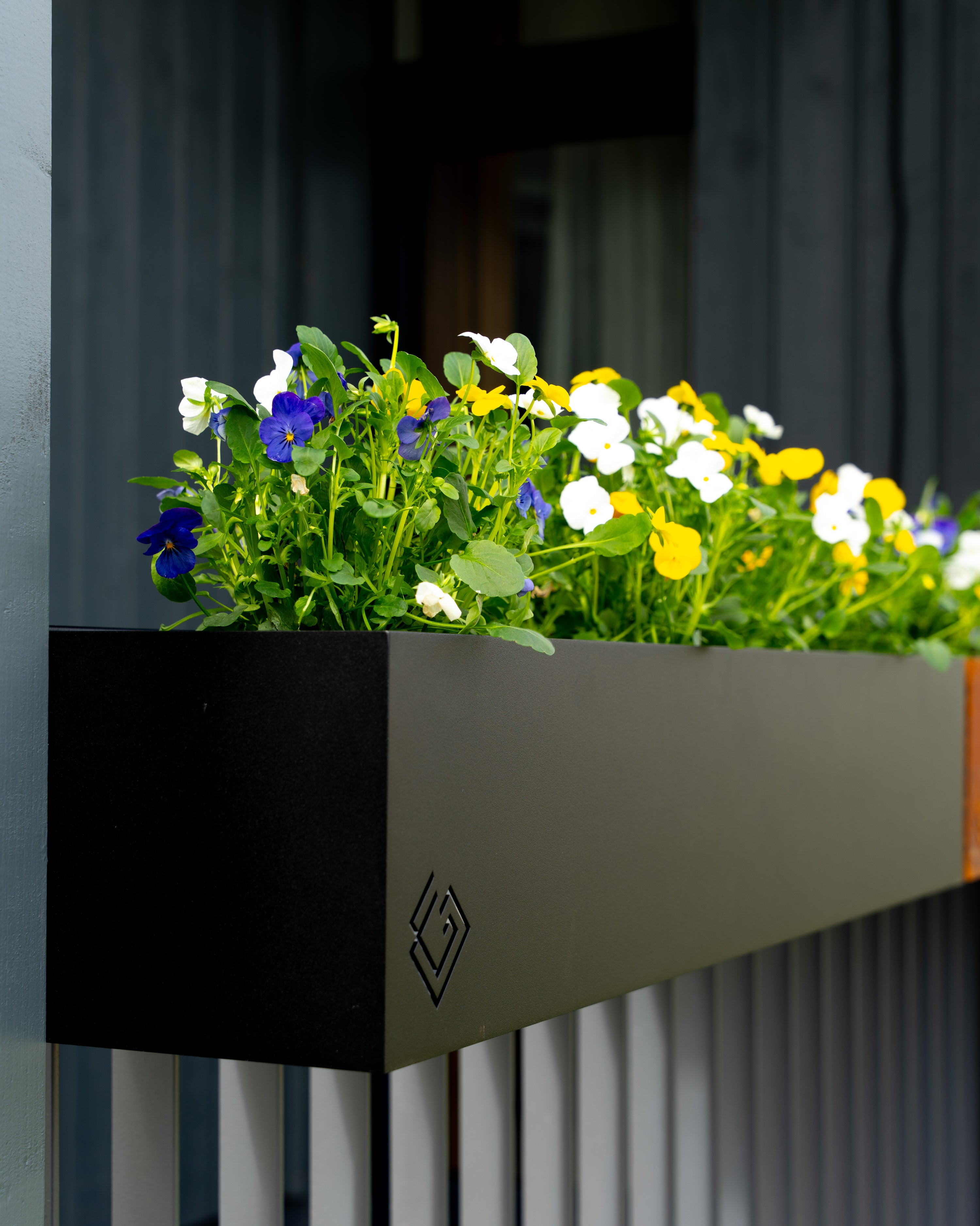 Melna metāla puķu kaste ar GG logo un puķēm